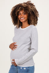 woman wearing a gray and white striped maternity top and holding her baby bump with a smile