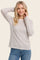 woman wearing a light beige long sleeve striped top and blue jeans, smiling with hands behind her head