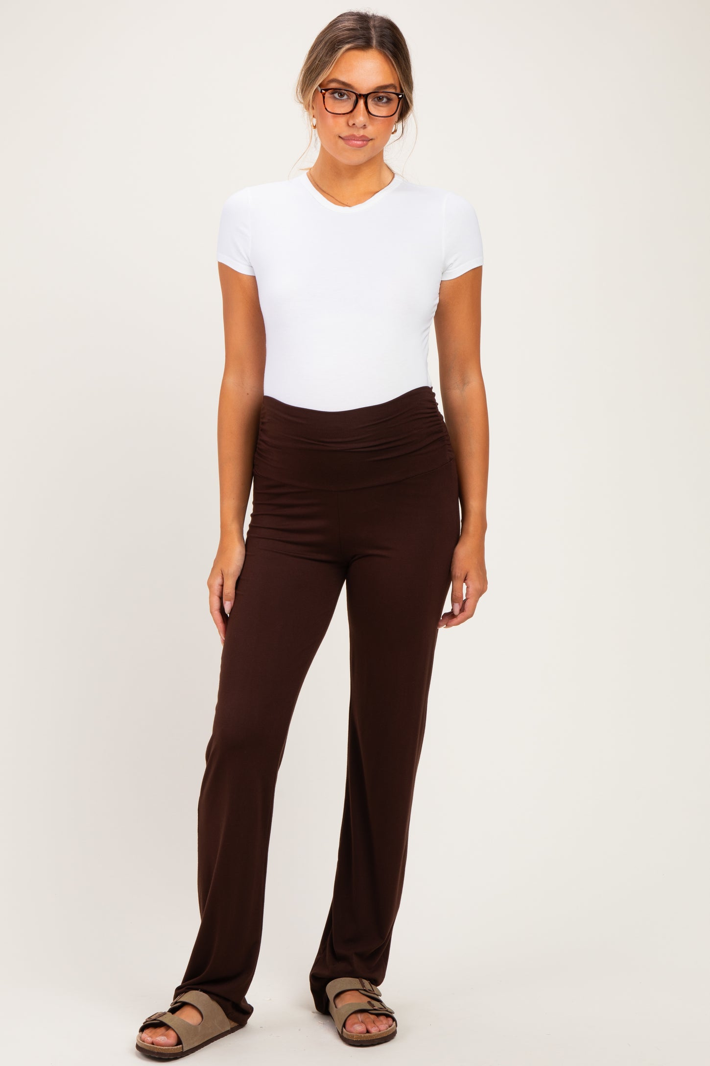 woman wearing a white short sleeve maternity top and brown maternity pants with a ruched waistband, showing a baby bump