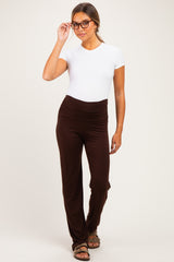woman wearing a white short sleeve maternity top and brown maternity pants, styled with glasses and a relaxed pose