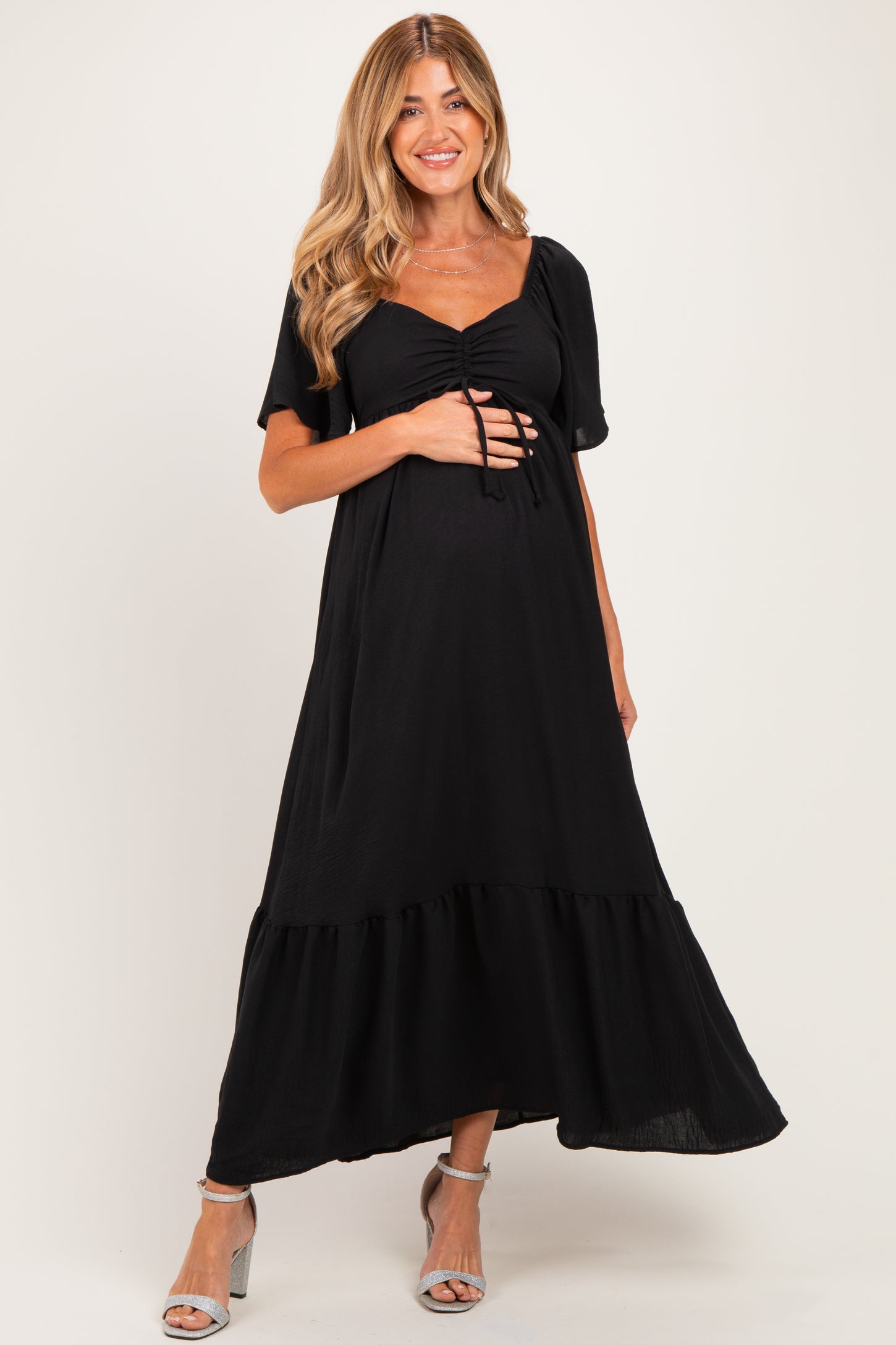 woman wearing a black maternity maxi dress with short sleeves and a ruffled hem, holding her baby bump