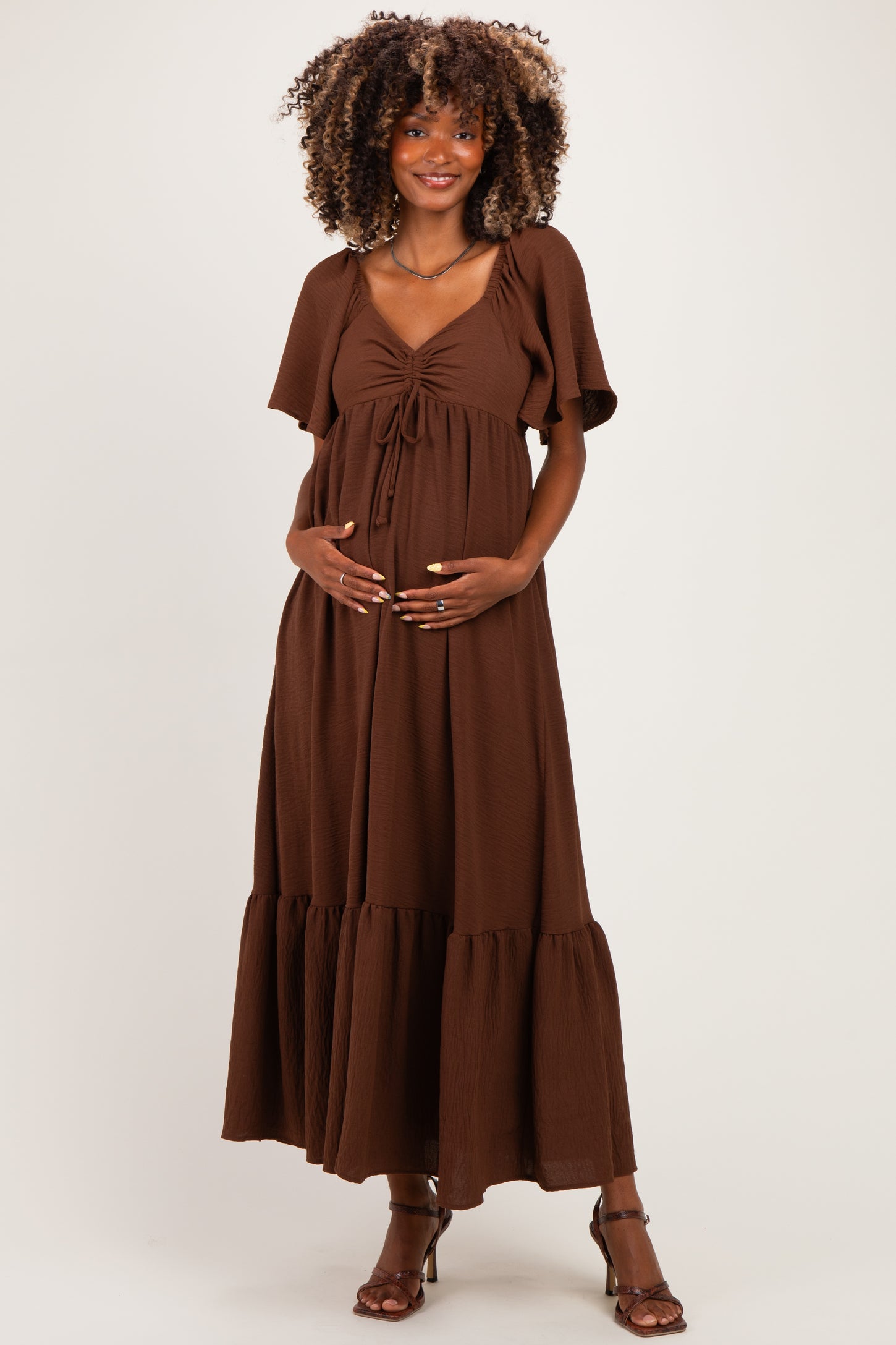 woman wearing a brown maternity maxi dress with puff sleeves and a tie-front detail, highlighting her baby bump