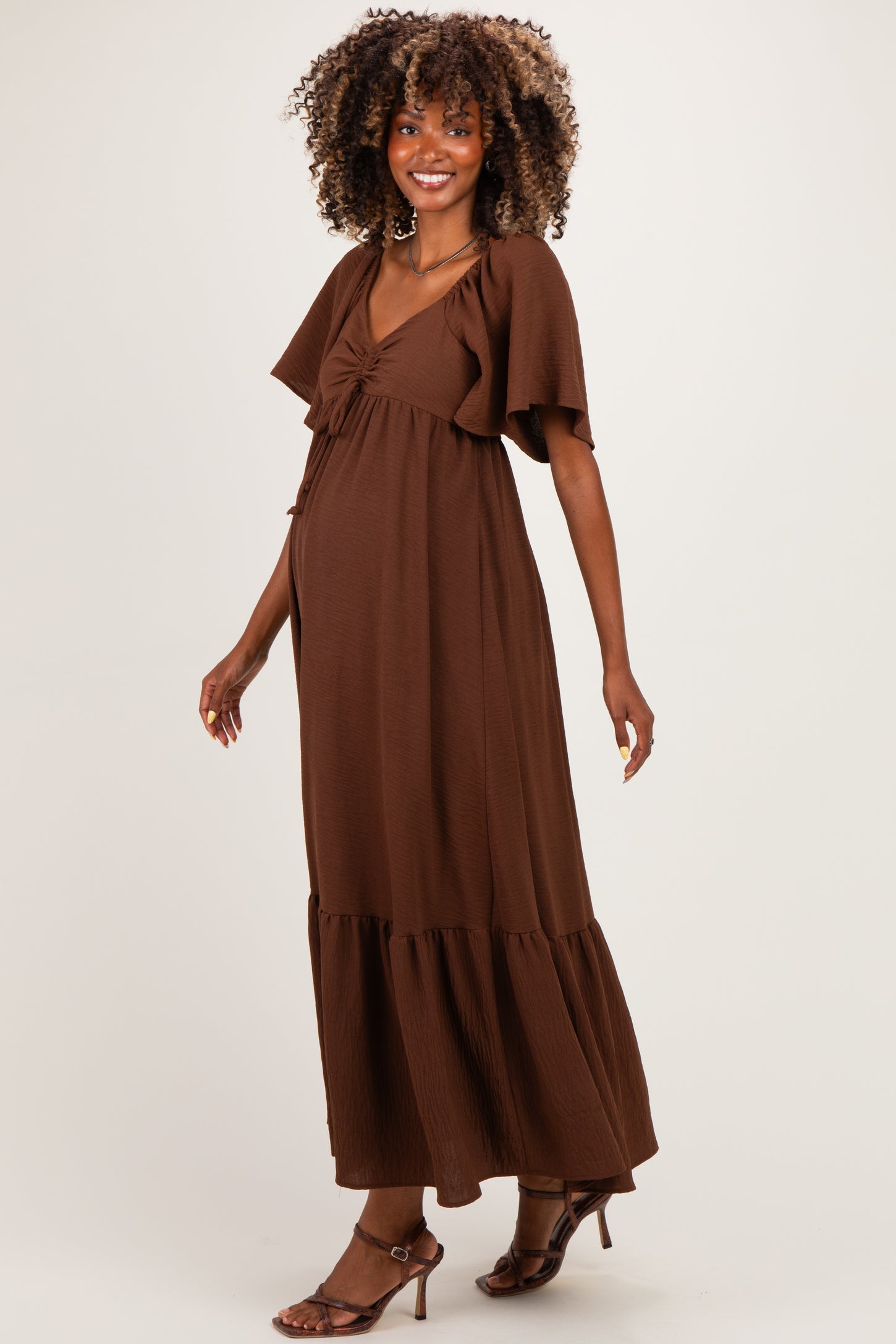 woman wearing a brown maternity maxi dress with flutter sleeves and a gathered waist, showcasing her baby bump