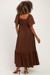 woman wearing a brown maternity maxi dress with short puff sleeves and a ruffled hem, showing her baby bump from the back