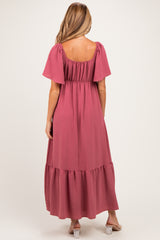 woman wearing a dusty pink maternity maxi dress with short sleeves and a tiered hem, showing off a baby bump from the back