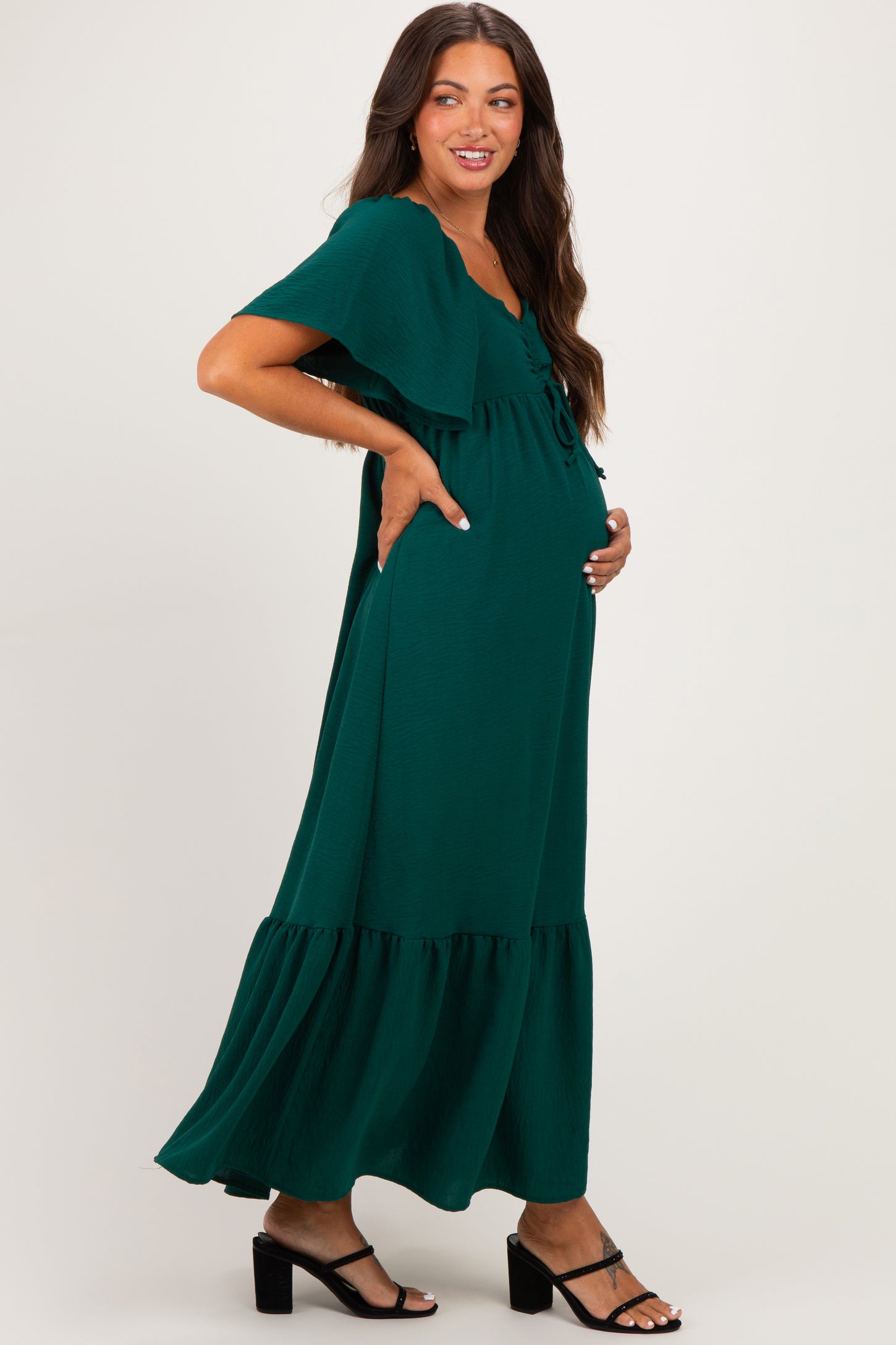 woman wearing a dark green maternity maxi dress with flutter sleeves and a baby bump visible