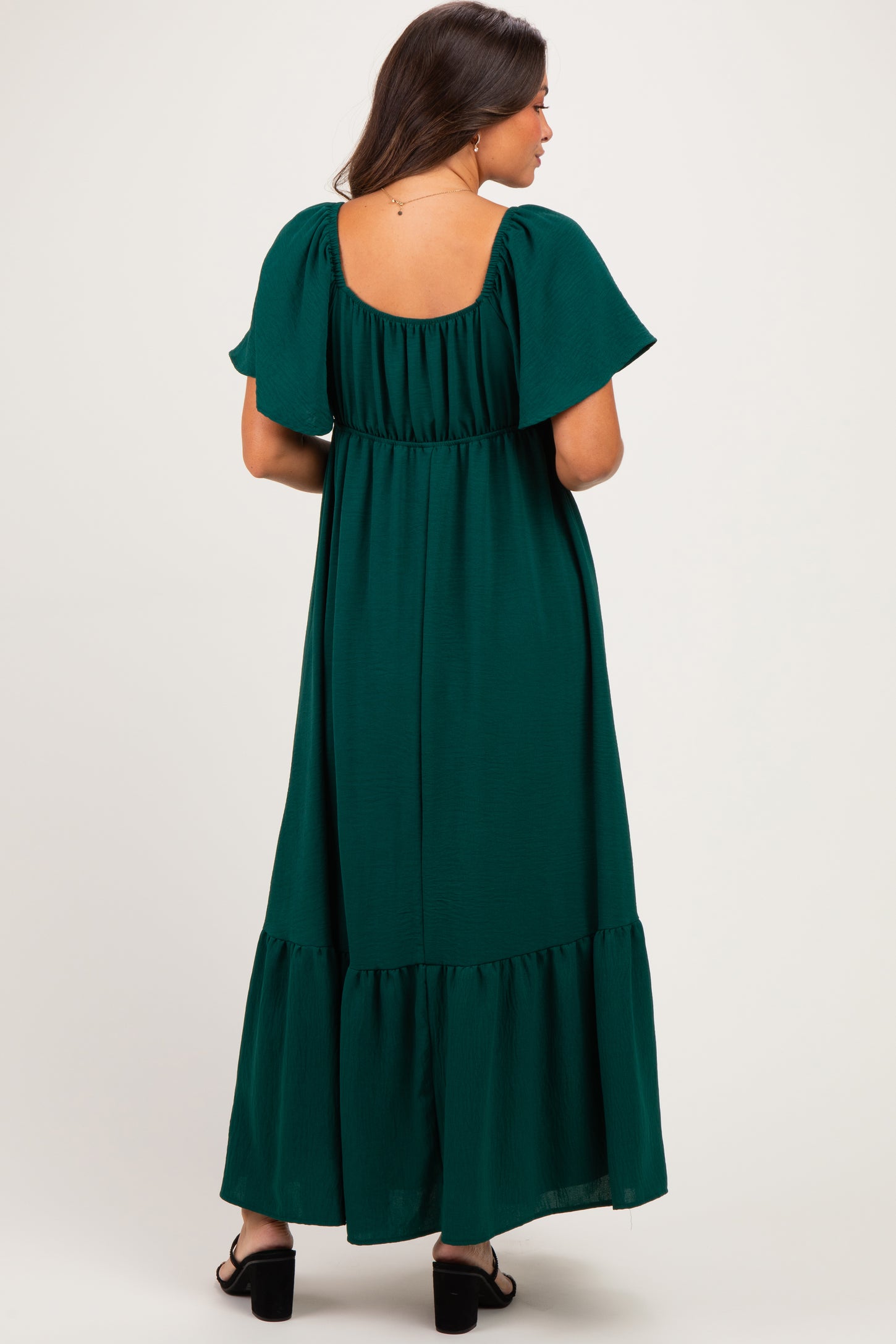 woman wearing a dark green maternity maxi dress with flutter sleeves and a tiered hem, showing a baby bump from the back