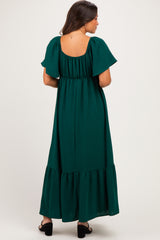woman wearing a dark green maternity maxi dress with flutter sleeves and a tiered hem, showing a baby bump from the back