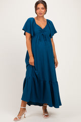 woman wearing a teal maternity maxi dress with a tie front and flutter sleeves, showcasing her baby bump