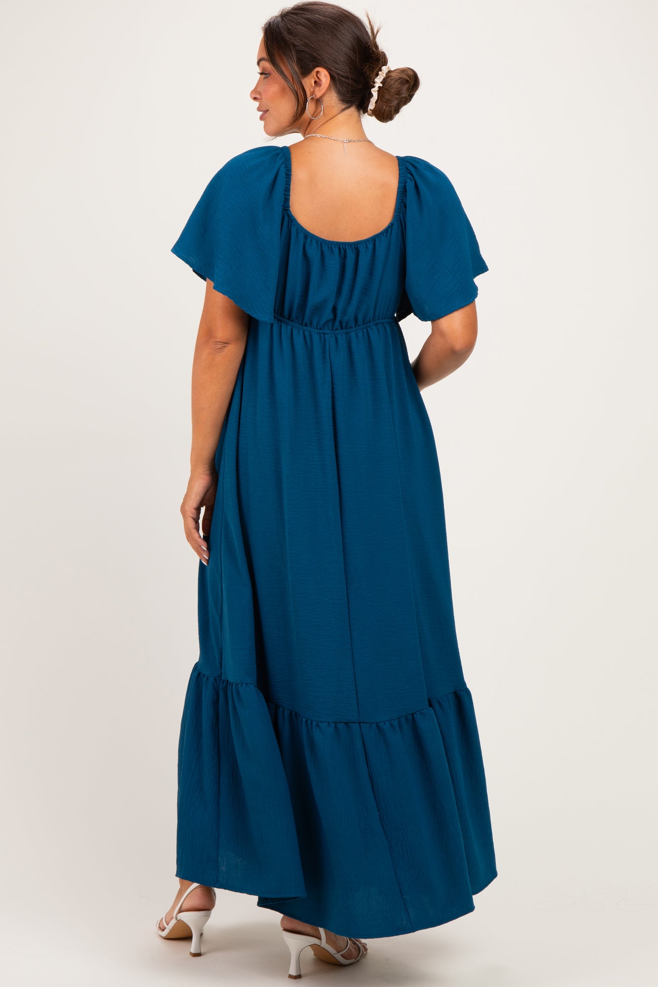 woman wearing a teal maternity maxi dress with flutter sleeves and a tiered hem, showing her baby bump from the back
