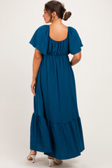 woman wearing a teal maternity maxi dress with flutter sleeves and a tiered hem, showing her baby bump from the back