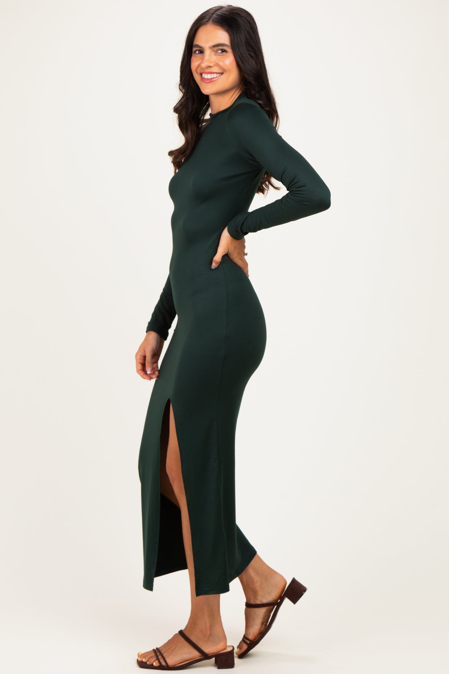 woman wearing a dark green long sleeve maxi dress with a side slit and brown sandals