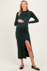 woman wearing a dark green long sleeve maternity dress with a thigh slit and holding her baby bump