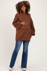 woman wearing a brown oversized maternity sweater and blue flared jeans, holding her baby bump
