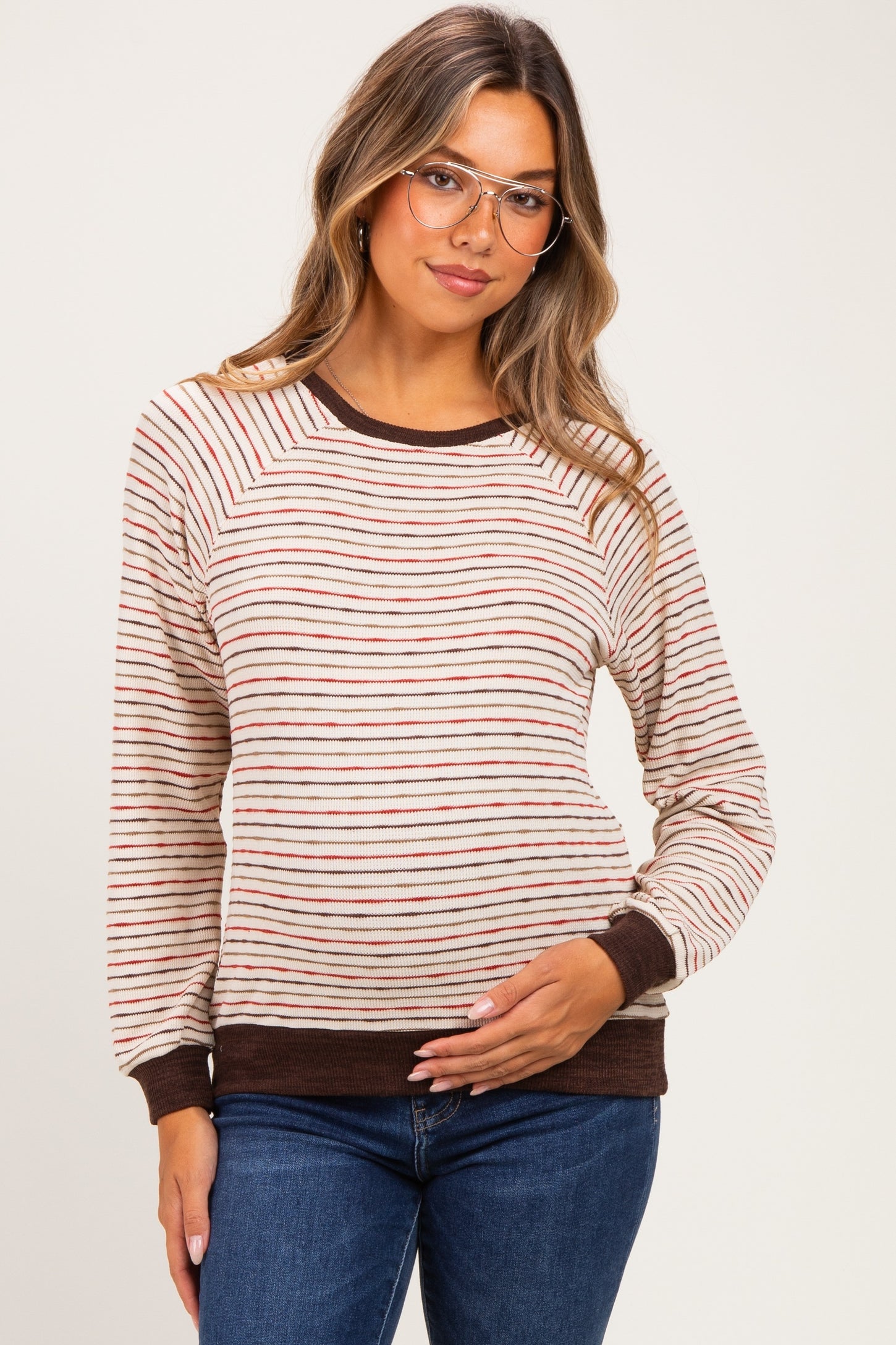 woman wearing a cream striped maternity top with long sleeves and a brown trim, holding her baby bump