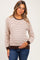 woman wearing a cream striped maternity top with long sleeves and a brown trim, holding her baby bump