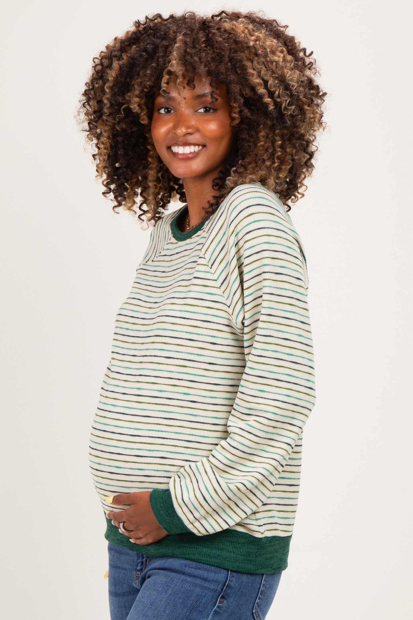 woman wearing a striped green and white maternity sweater with a visible baby bump, smiling at the camera