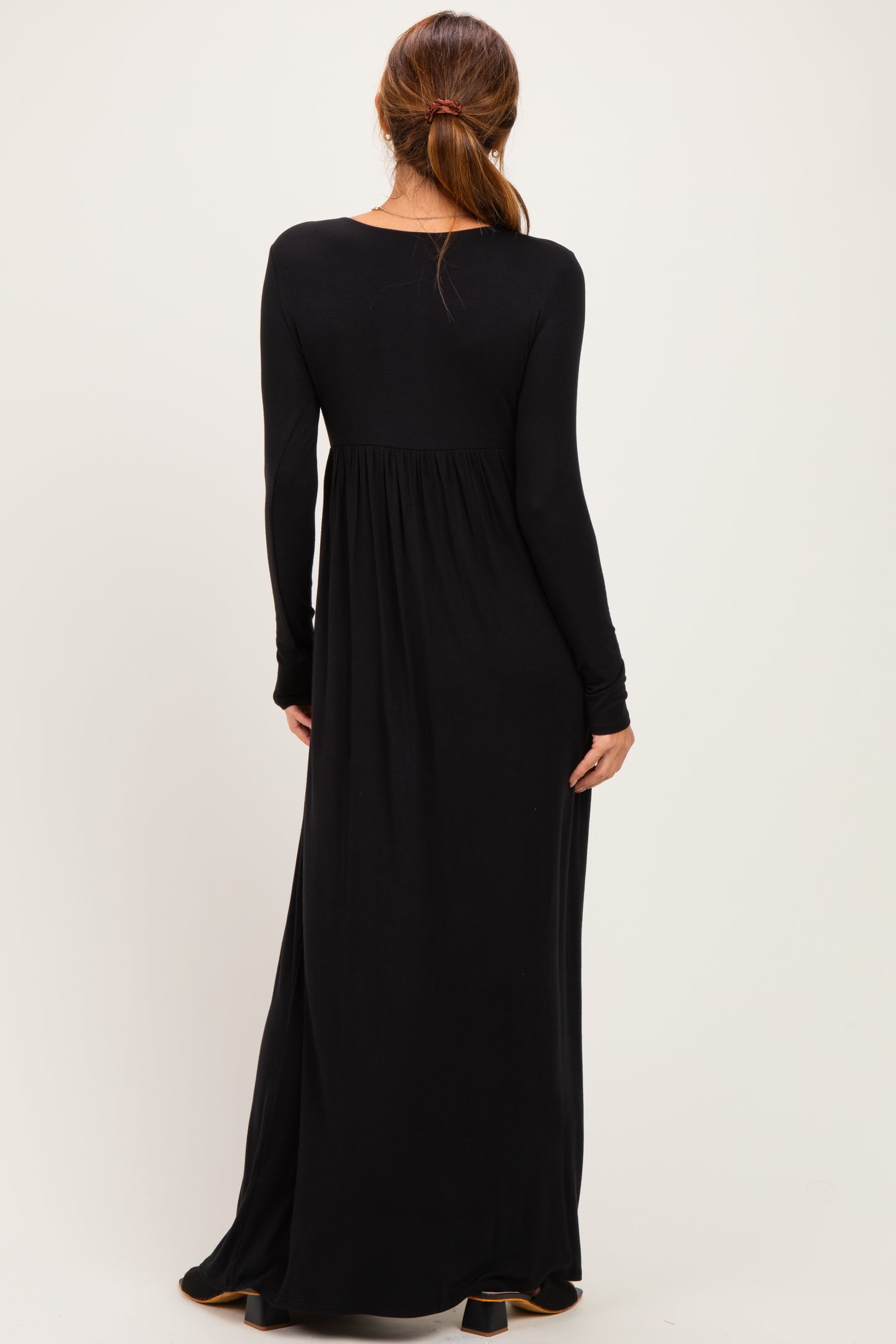woman wearing a long black maxi dress with long sleeves and a fitted bodice, showing the back view