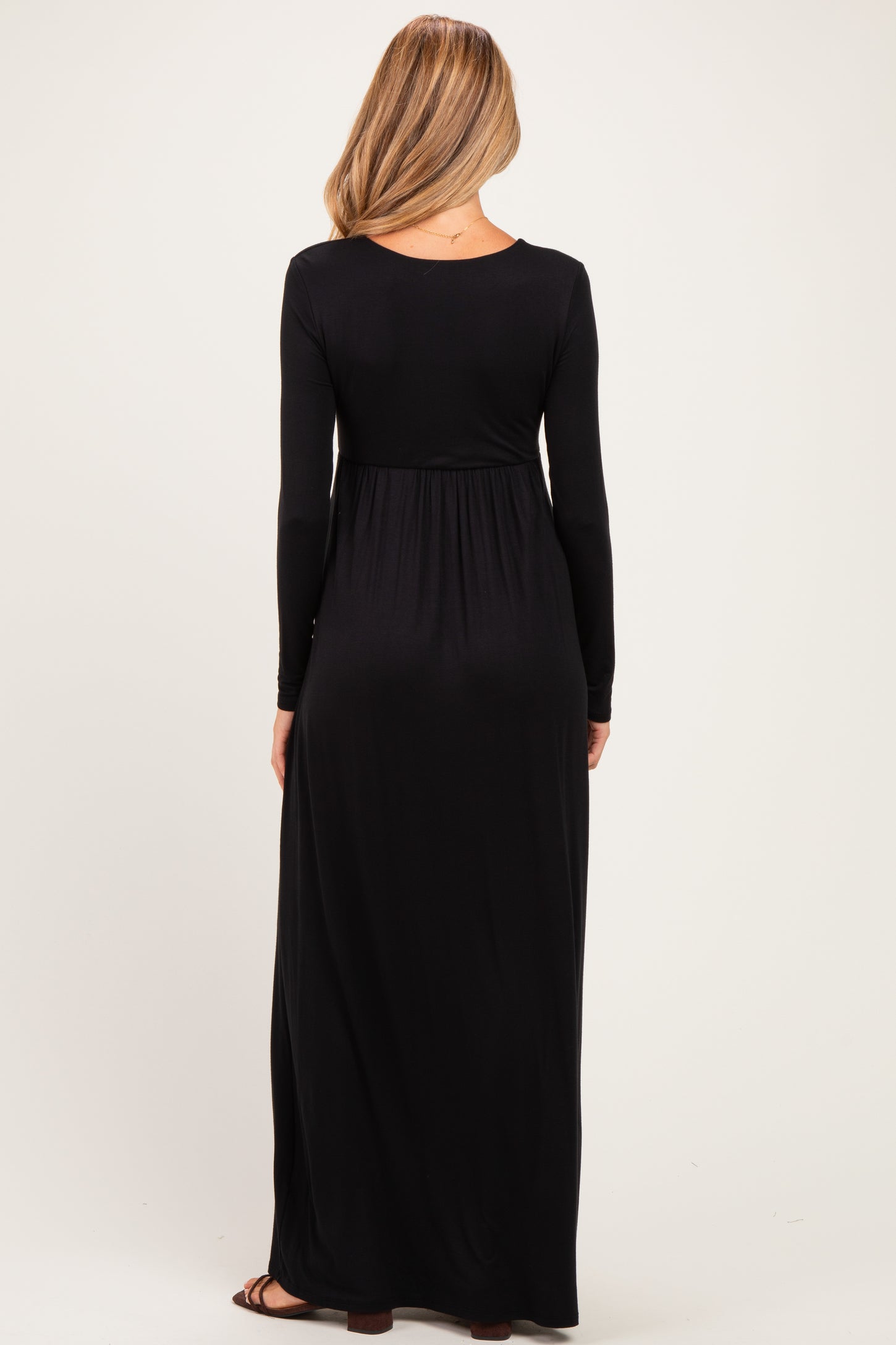 woman wearing a long black maternity maxi dress, showing the back view and fitted under the bust with a flowing skirt