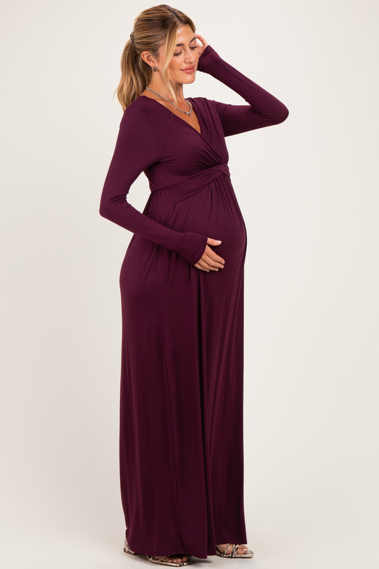 woman wearing a burgundy long sleeve maternity dress and gently holding her baby bump