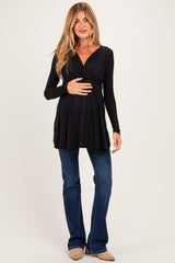 woman wearing a black long sleeve maternity top and holding her baby bump with blue jeans and beige ankle boots