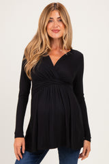 woman wearing a black long sleeve maternity top with a wrap design and a visible baby bump