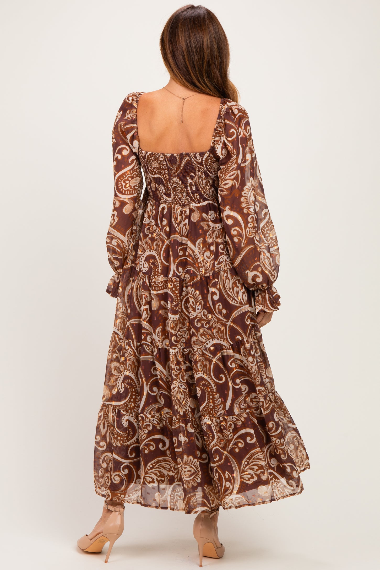 woman wearing a brown floral maxi dress with long sleeves and a tiered skirt, viewed from the back