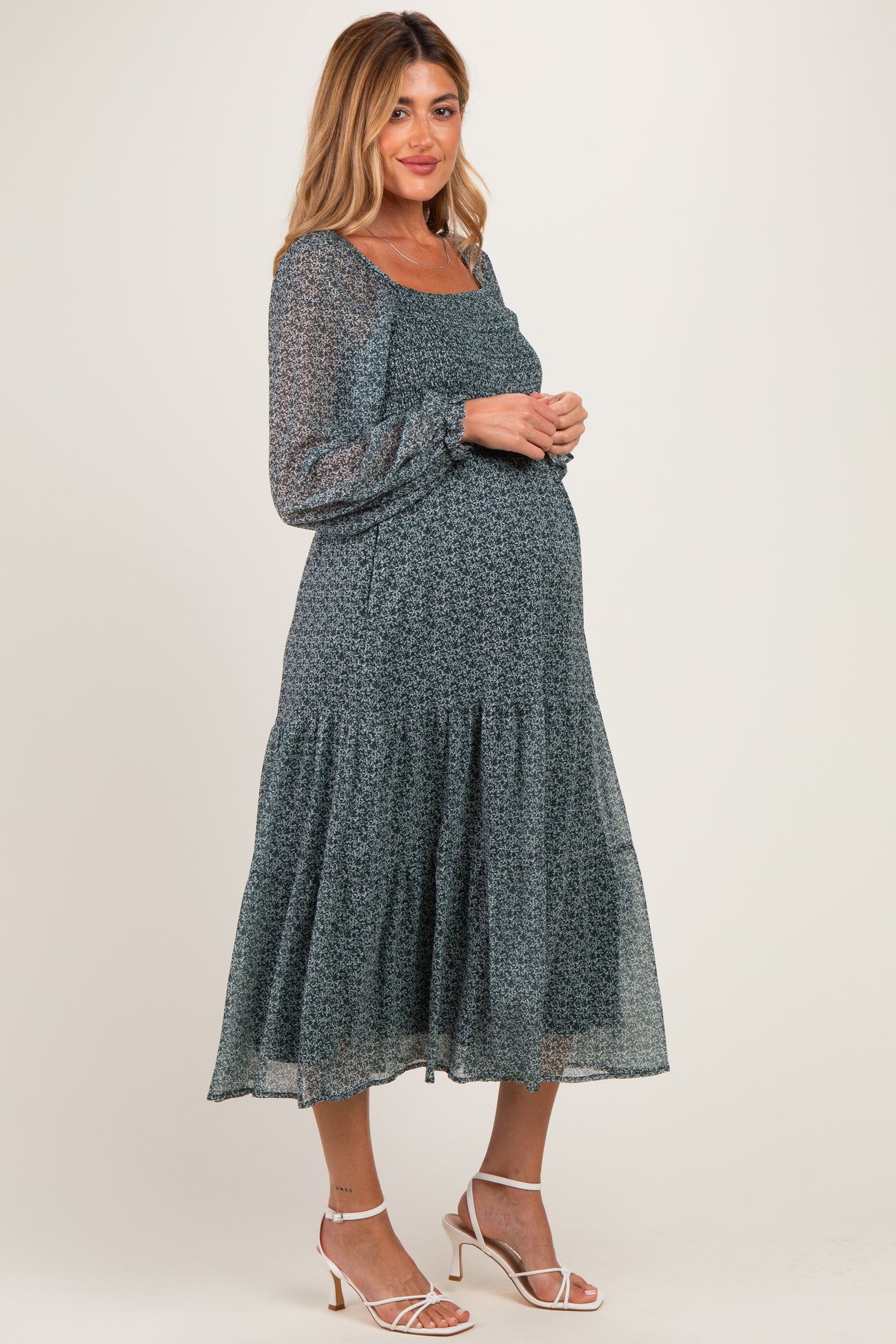 woman wearing a teal floral long sleeve maternity dress with tiered skirt and holding her baby bump