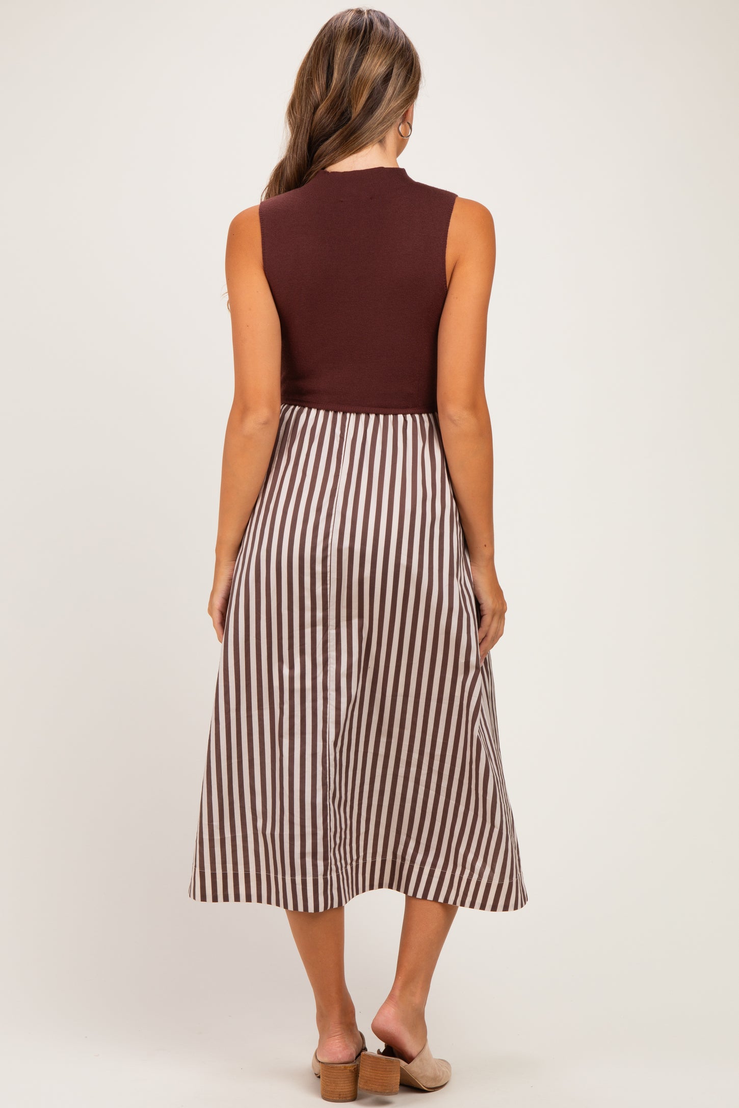 woman wearing a burgundy sleeveless maternity dress with a striped skirt, showing her back and a flowing silhouette
