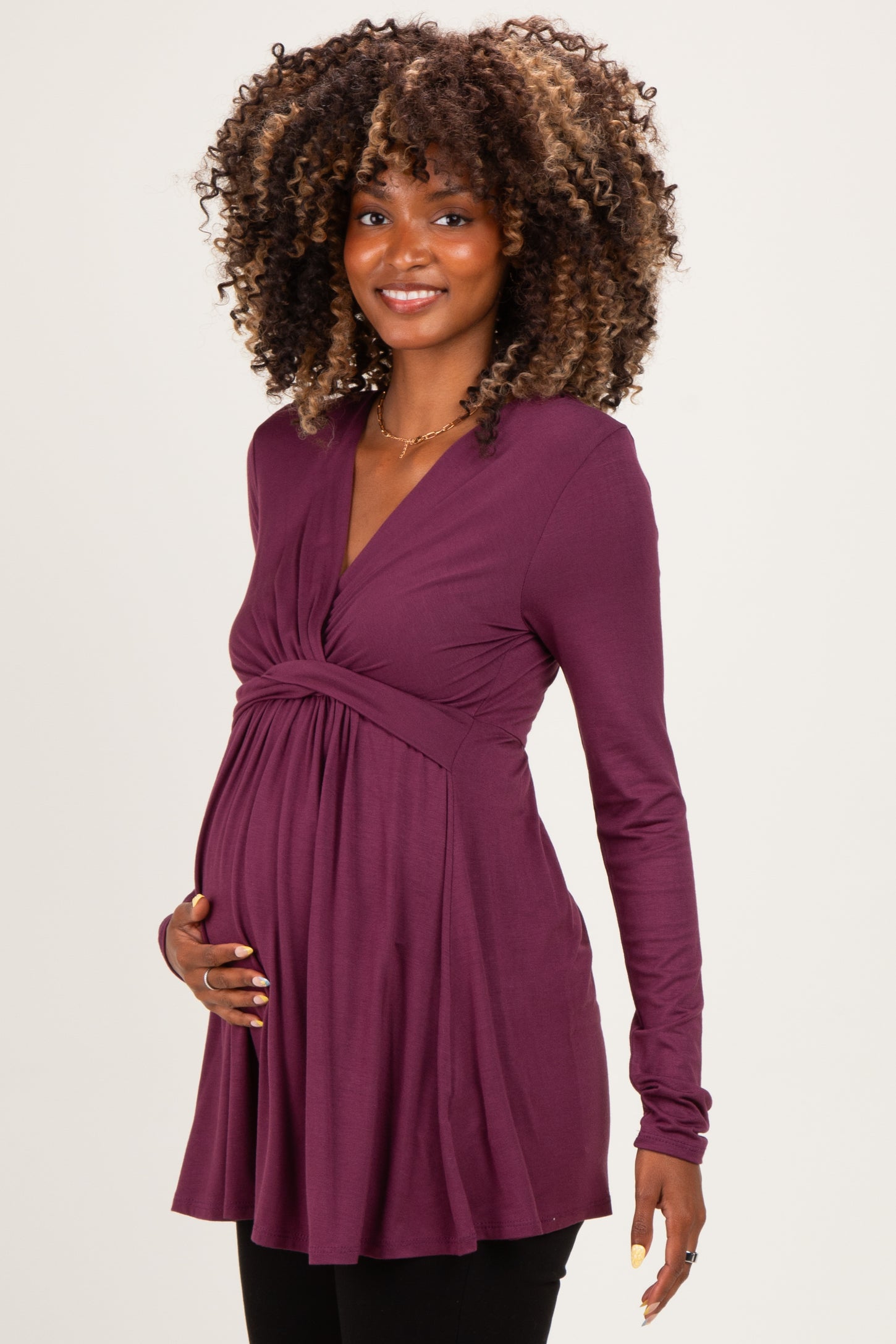 woman wearing a purple long sleeve maternity top and holding her baby bump