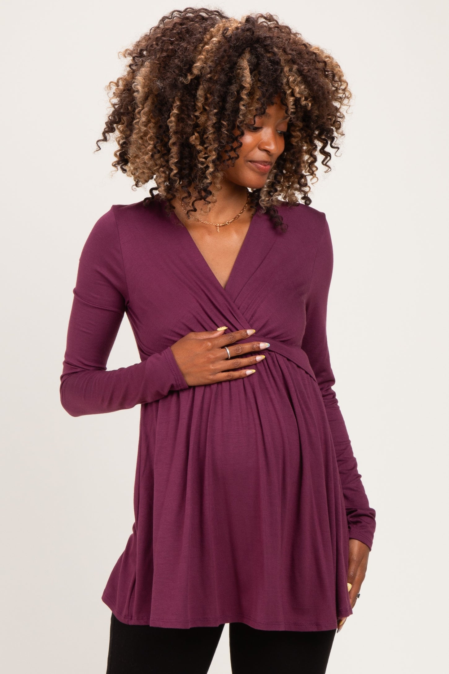 woman wearing a purple long sleeve maternity top and holding her baby bump