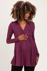 woman wearing a purple long sleeve maternity top and holding her baby bump