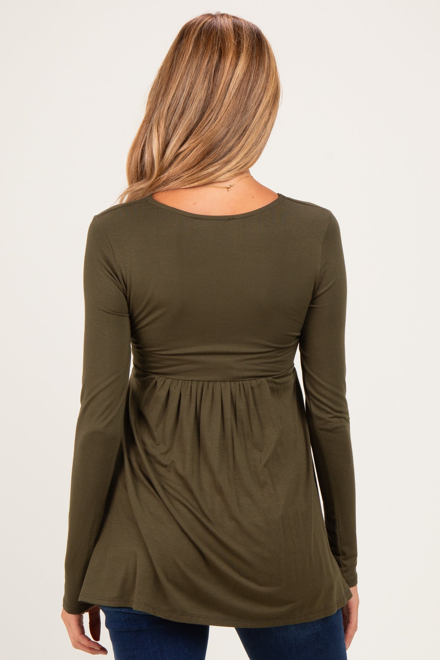 woman wearing a dark green long sleeve maternity top with a gathered waist and a relaxed fit from the back