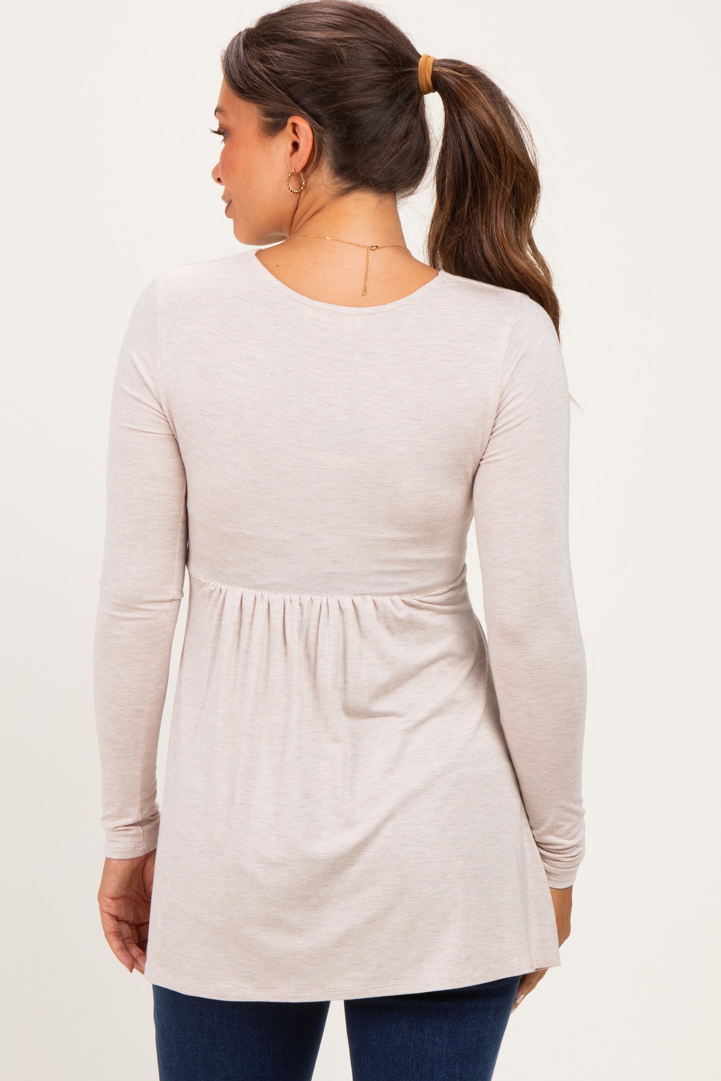 woman wearing a light beige long sleeve maternity top with a gathered waist and flowing silhouette, showing her back