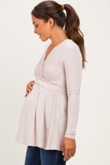 woman wearing a light pink long sleeve maternity top, gently holding her baby bump, styled with a flared silhouette