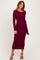 woman wearing a burgundy long sleeve midi dress with a twist detail at the waist and strappy heels