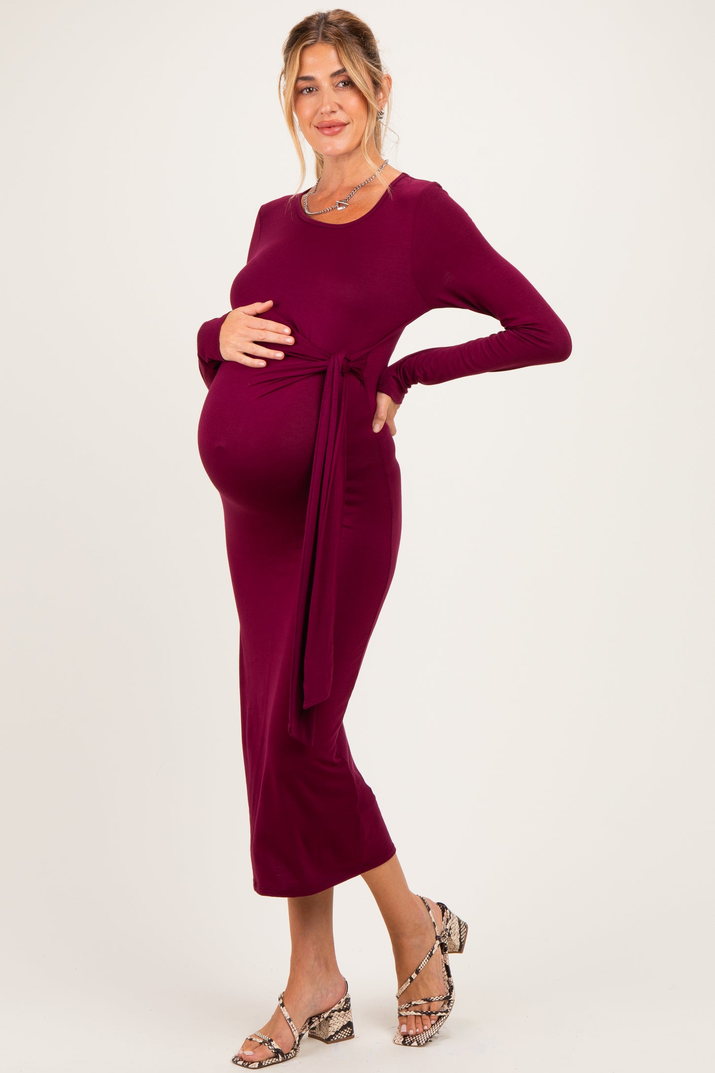 woman wearing a burgundy long sleeve maternity dress with a tie at the waist, showcasing her baby bump