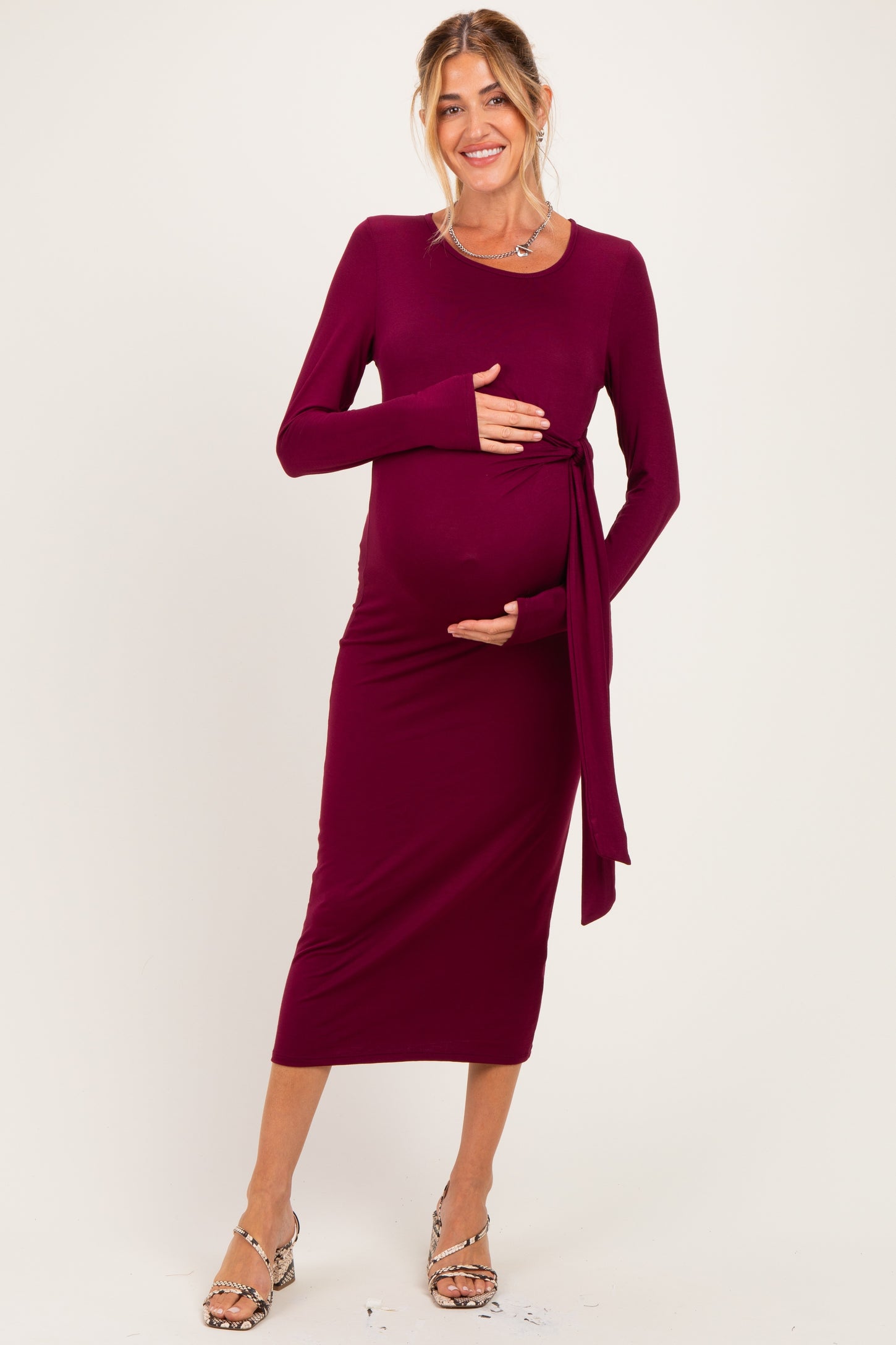 woman wearing a burgundy long sleeve maternity dress with a tied waist holding her baby bump