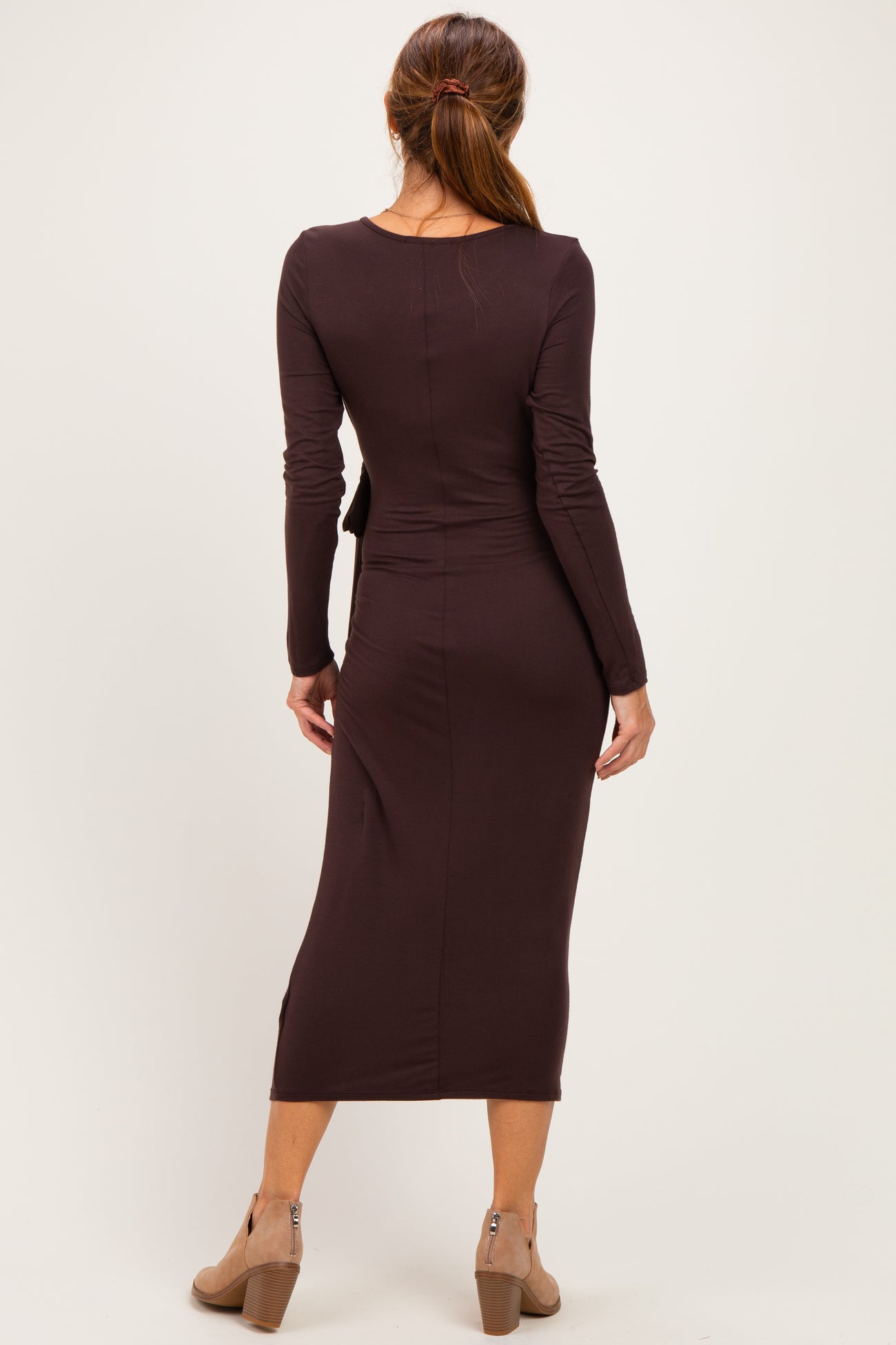 woman wearing a brown long sleeve fitted dress with a midi length and a back slit, standing and facing away from the camera