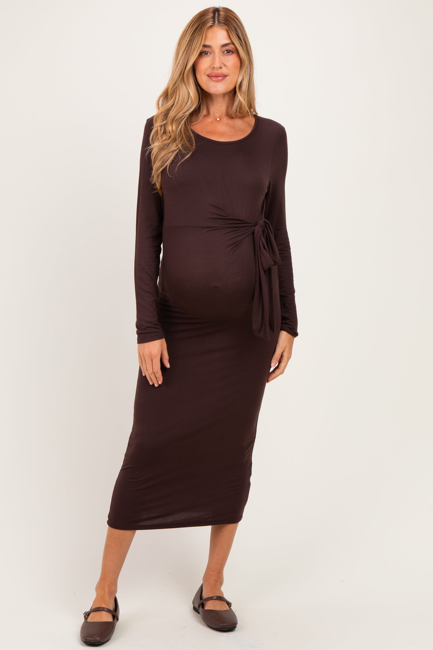 woman wearing a dark brown maternity dress with a side tie detail and long sleeves, showcasing her baby bump