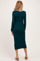 woman wearing a dark teal long sleeve maternity dress that hugs the body and falls to mid-calf, showing a baby bump