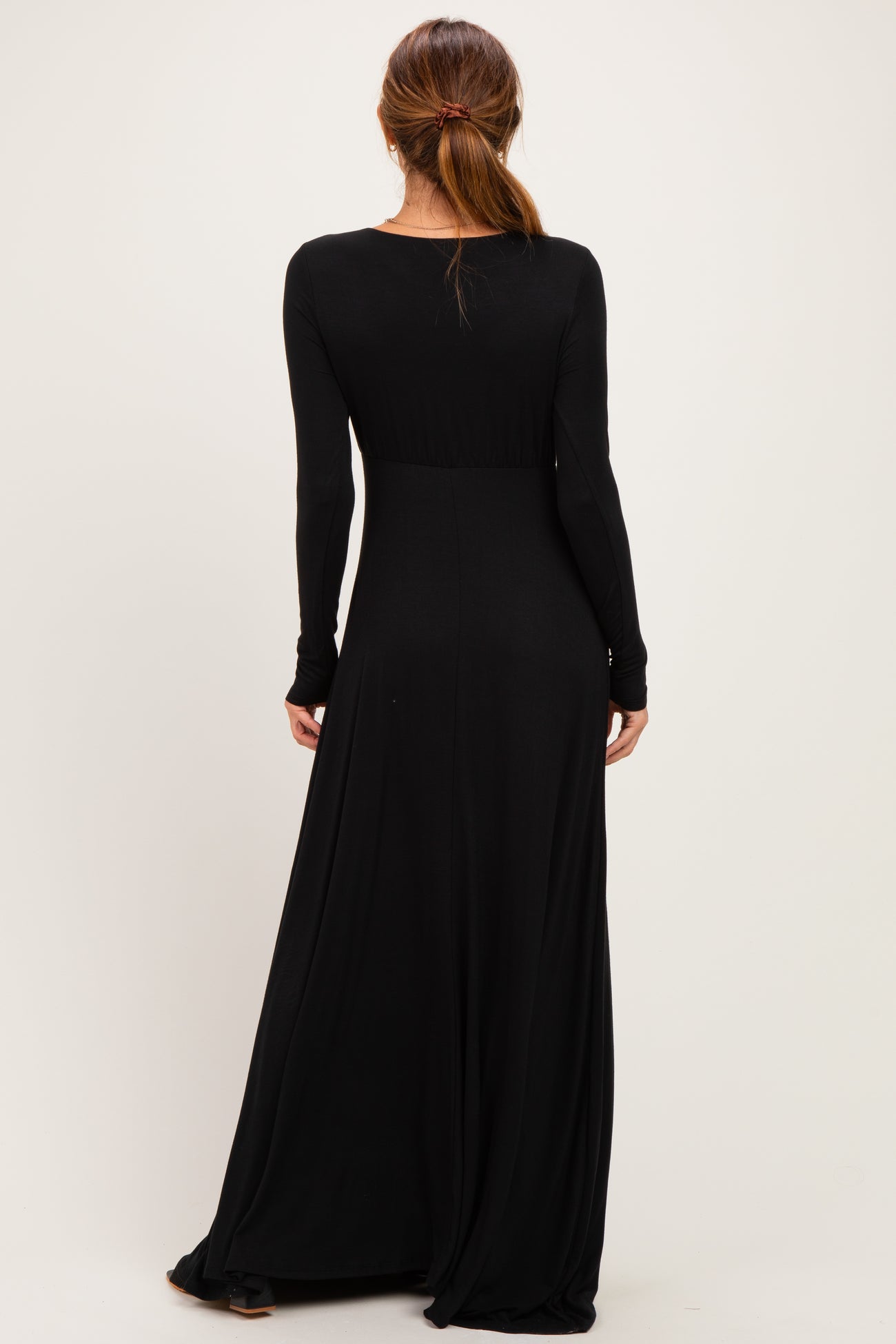 woman wearing a fitted black long sleeve maxi dress, showing the back view and flowing skirt
