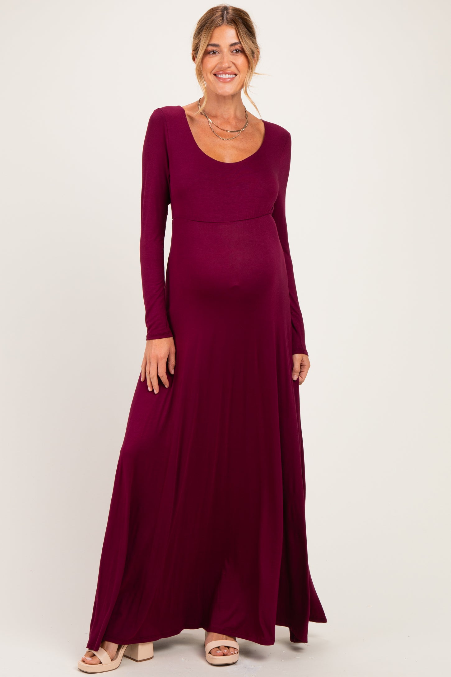 woman wearing a maroon long sleeve maternity maxi dress with a scoop neckline and visible baby bump