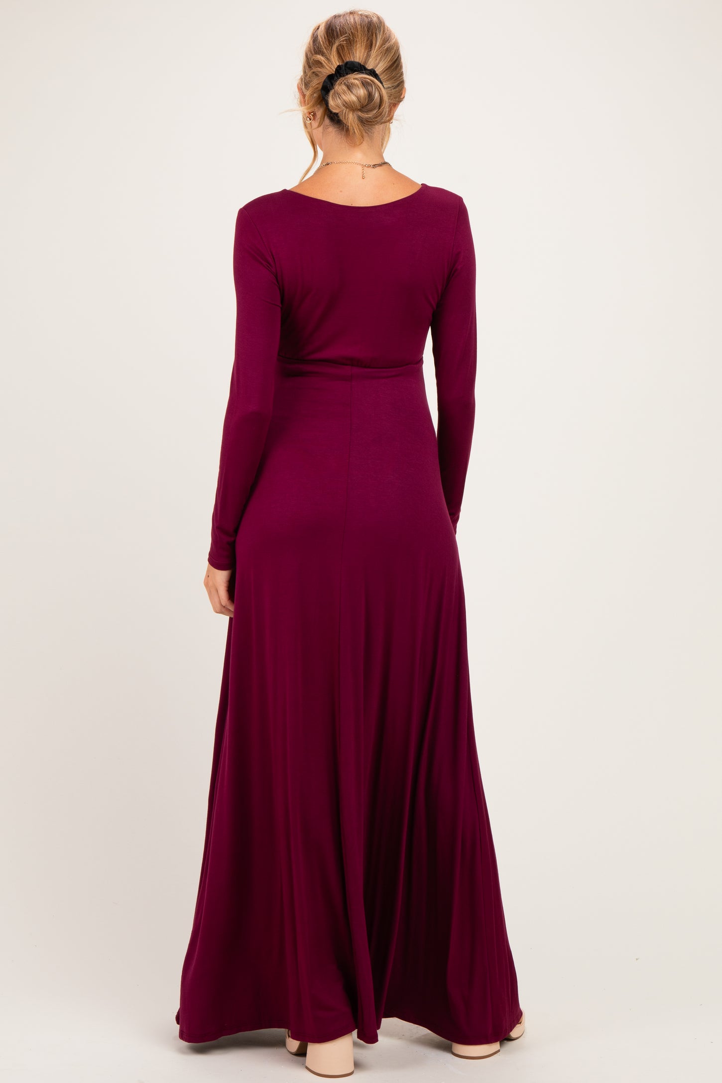 woman wearing a long sleeve burgundy maternity maxi dress, styled with a flowing skirt and fitted bodice
