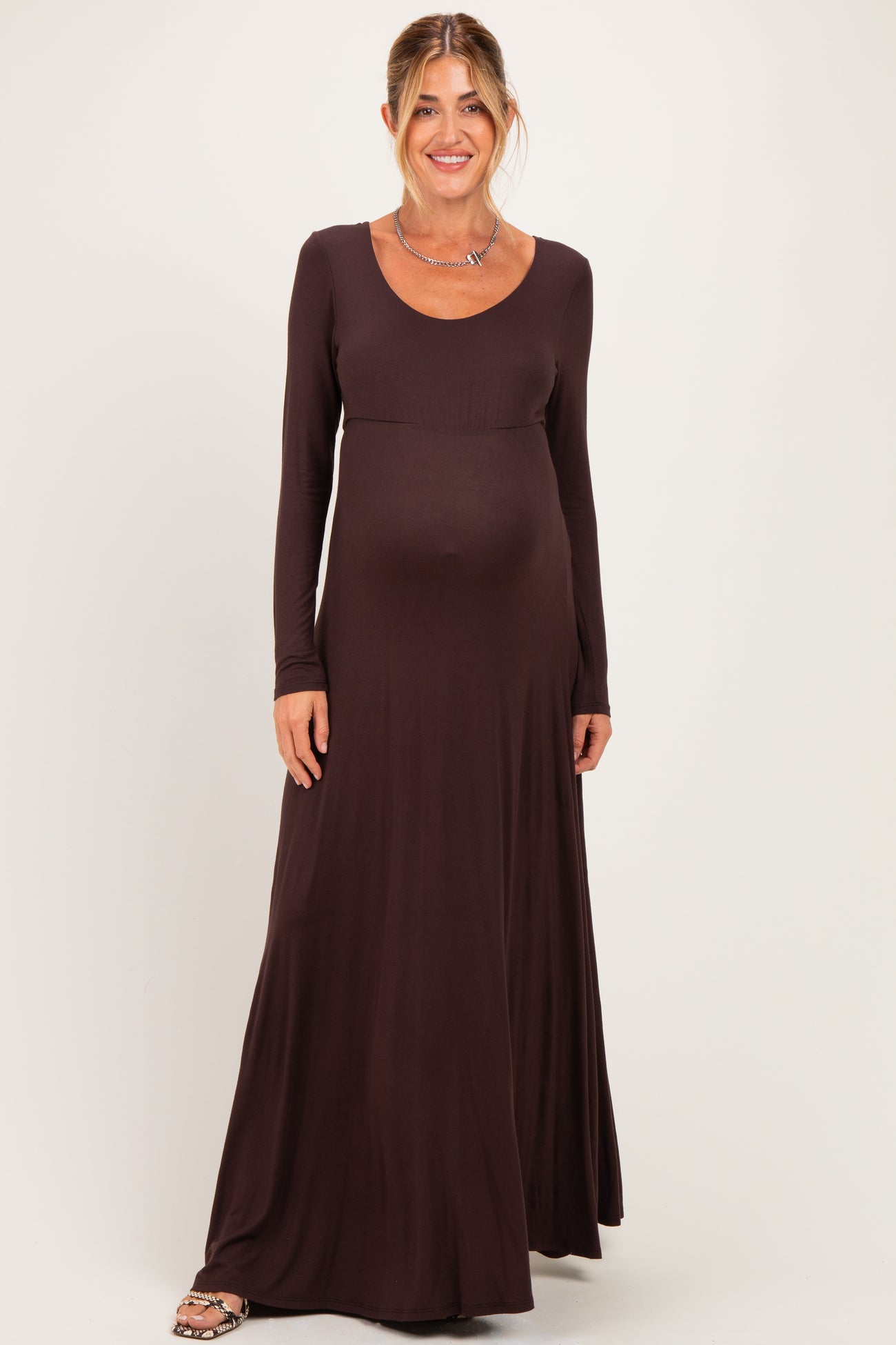 woman wearing a long sleeve brown maternity dress with a fitted bodice and flowy skirt, baby bump visible