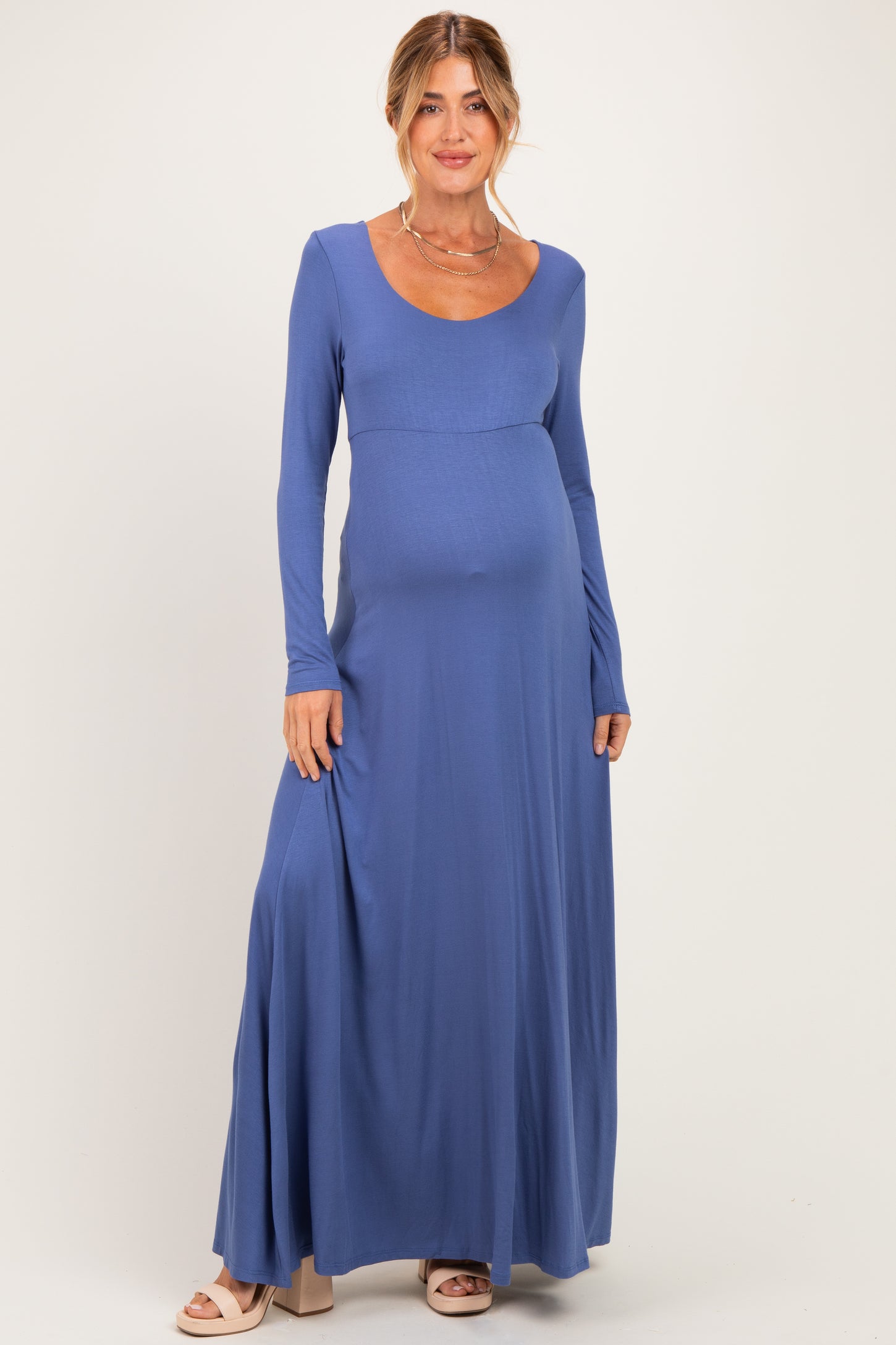 woman wearing a long sleeve blue maternity maxi dress with a fitted bodice and flowing skirt, showing her baby bump