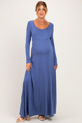 woman wearing a long sleeve blue maternity maxi dress with a fitted bodice and flowing skirt, showing her baby bump
