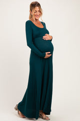 woman wearing a teal long sleeve maternity dress and cradling her baby bump