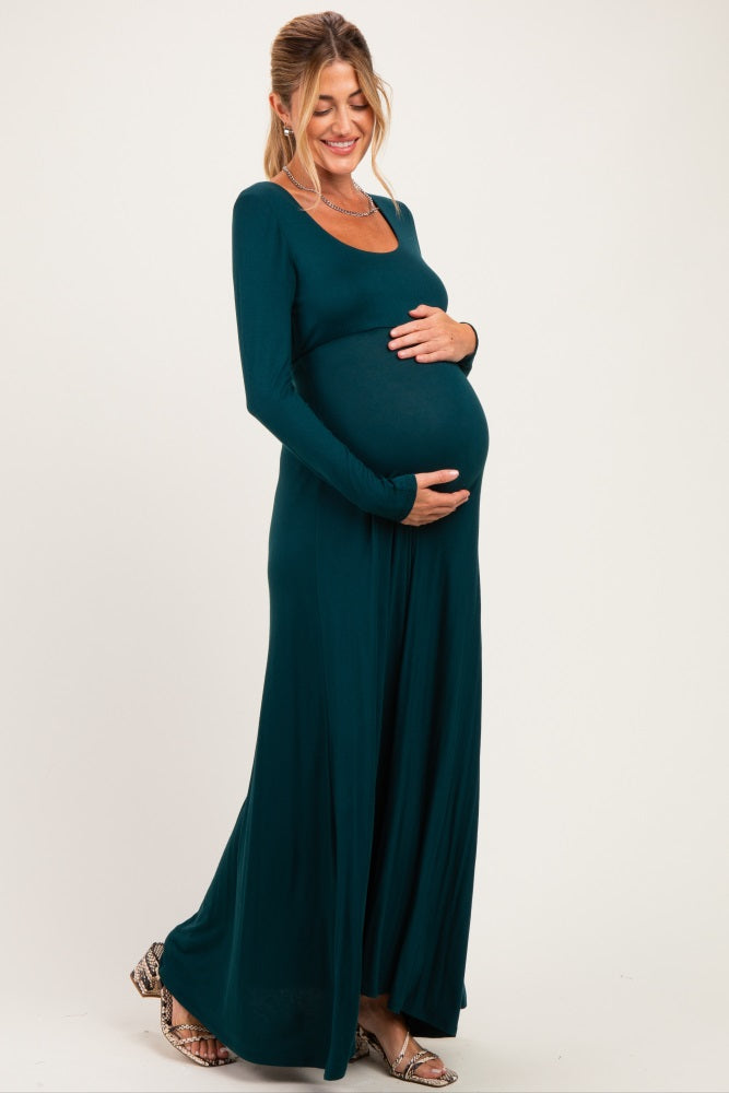 woman wearing a teal long sleeve maternity dress and cradling her baby bump