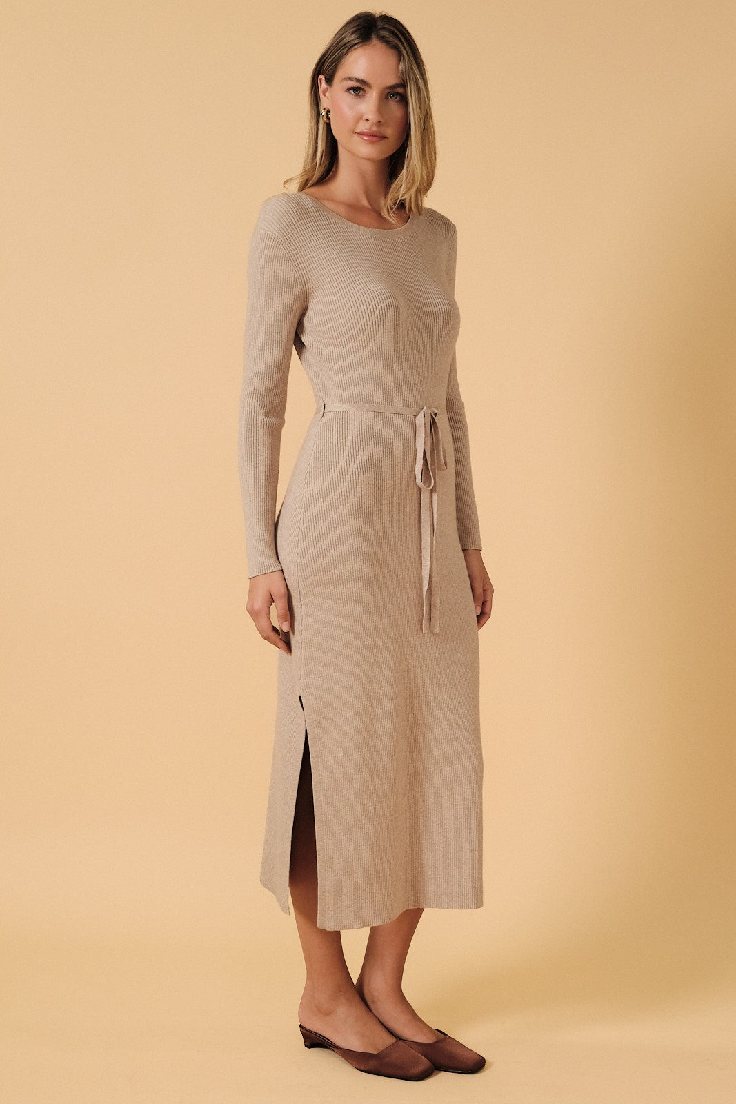 woman wearing a beige ribbed knit long sleeve dress with a side slit and a tie waist detail